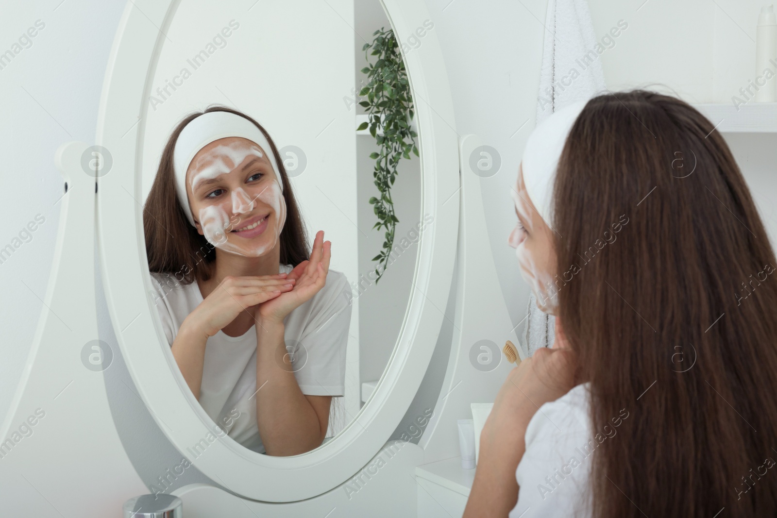 Photo of Teenage girl with cleansing foam on her face near mirror indoors. Acne treatment