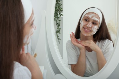 Photo of Teenage girl with cleansing foam on her face near mirror indoors. Acne treatment