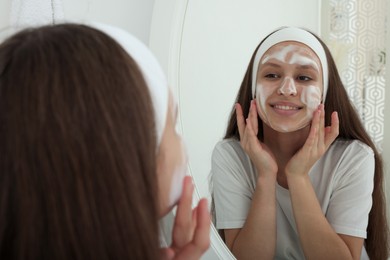 Photo of Teenage girl applying cleansing foam onto her face near mirror indoors. Acne treatment