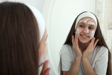 Photo of Teenage girl applying cleansing foam onto her face near mirror indoors. Acne treatment