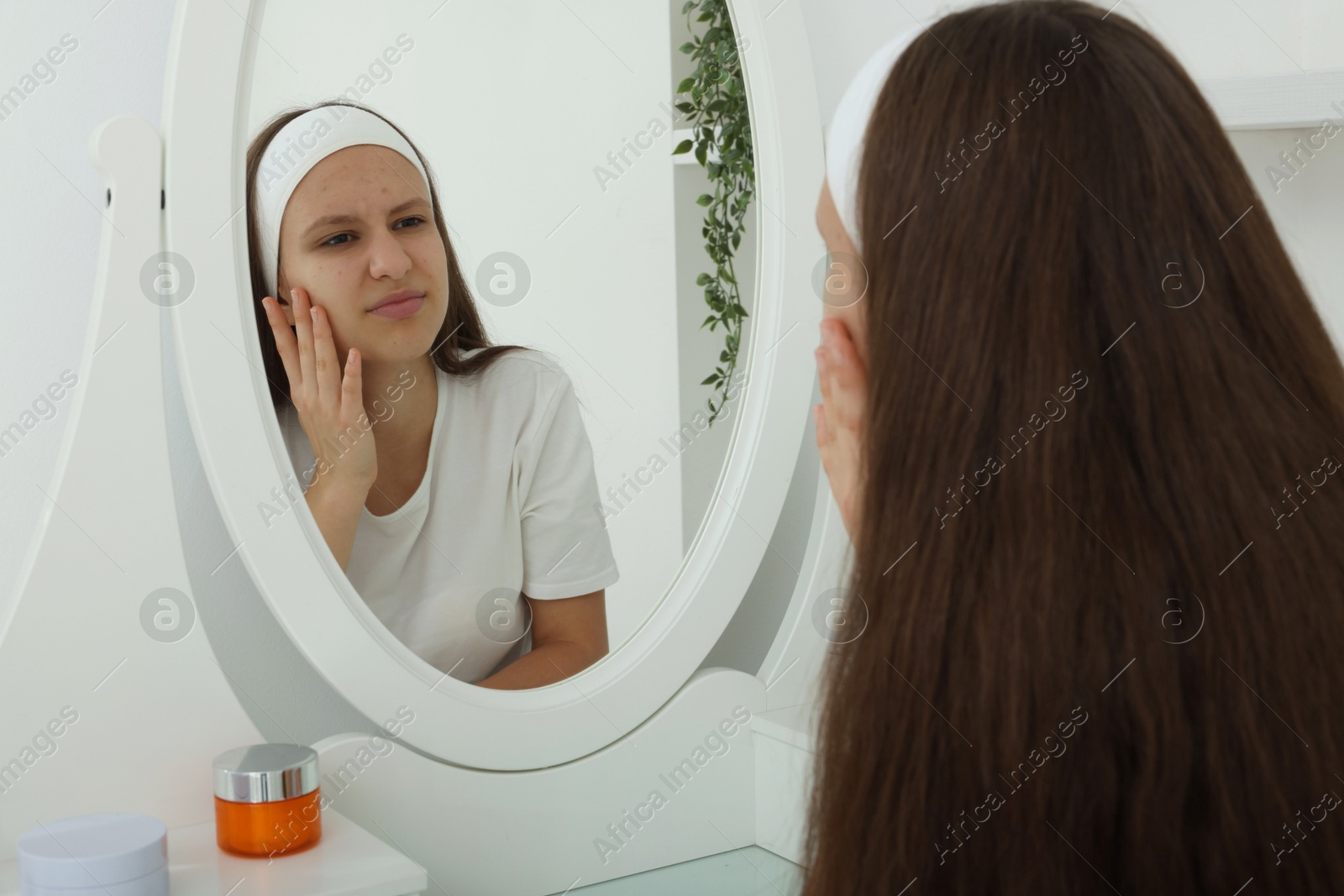 Photo of Upset teenage girl with acne problem looking in mirror indoors