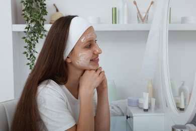 Photo of Teenage girl with cream on her face looking in mirror at home. Acne treatment