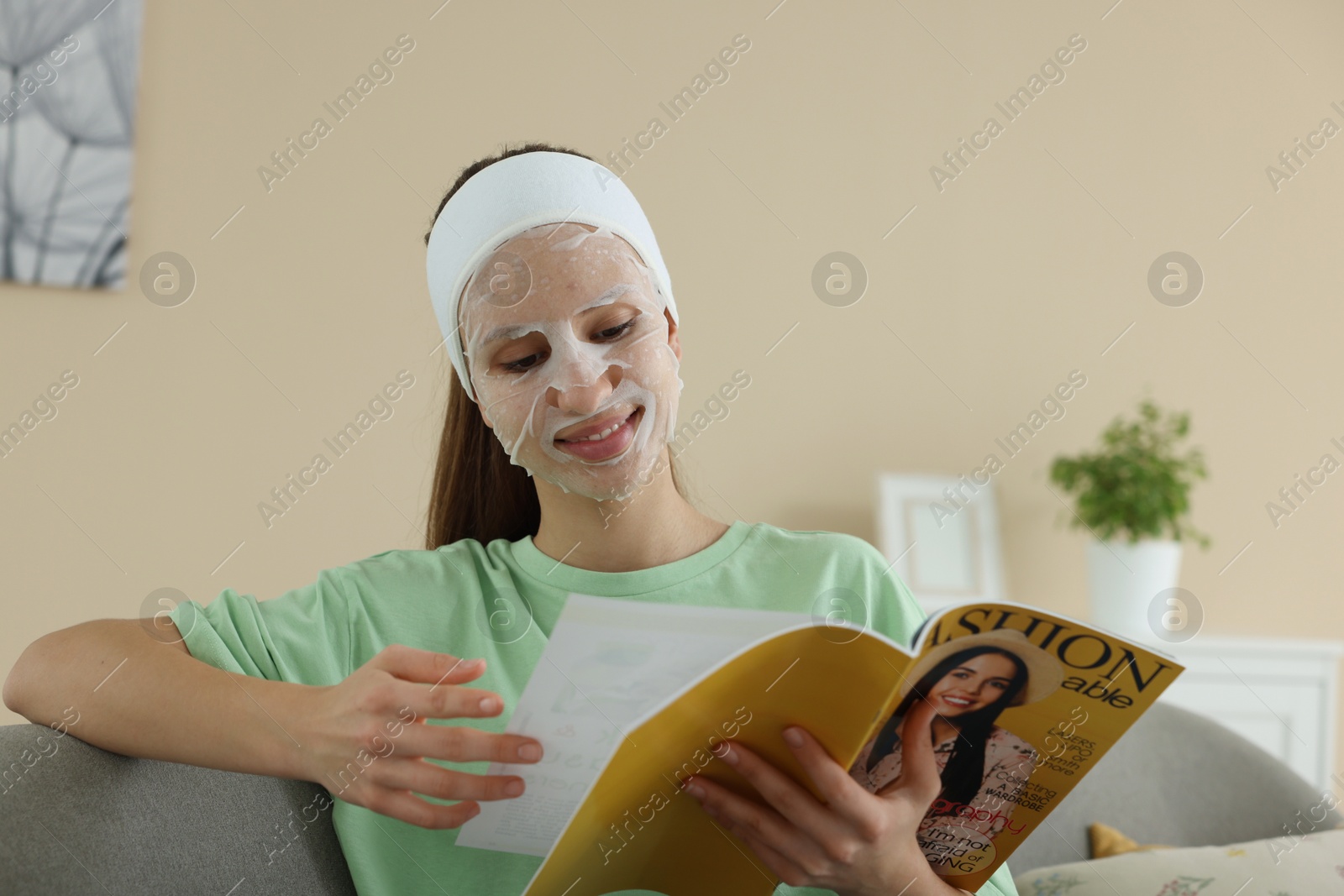 Photo of Teenage girl with sheet facial mask reading magazine at home. Acne treatment