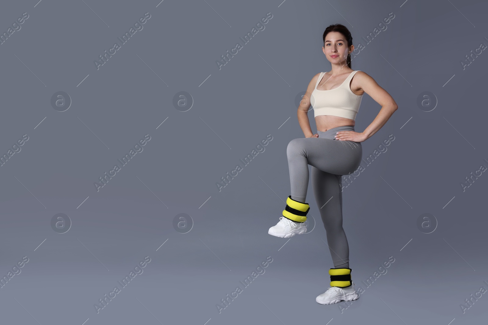 Photo of Woman in sportswear exercising with ankle weights on grey background, space for text