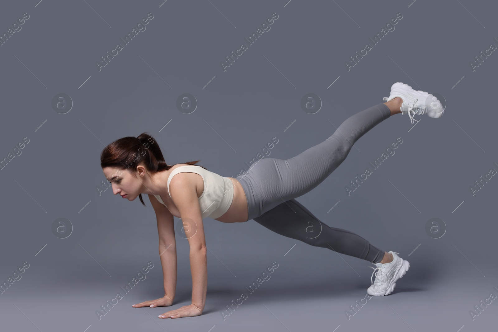 Photo of Woman in sportswear exercising on grey background