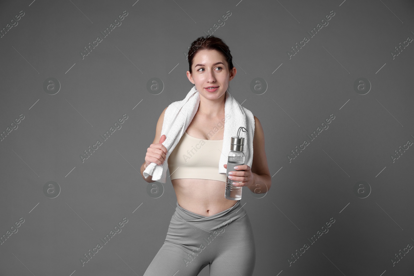 Photo of Woman in sportswear with bottle of water and towel on grey background