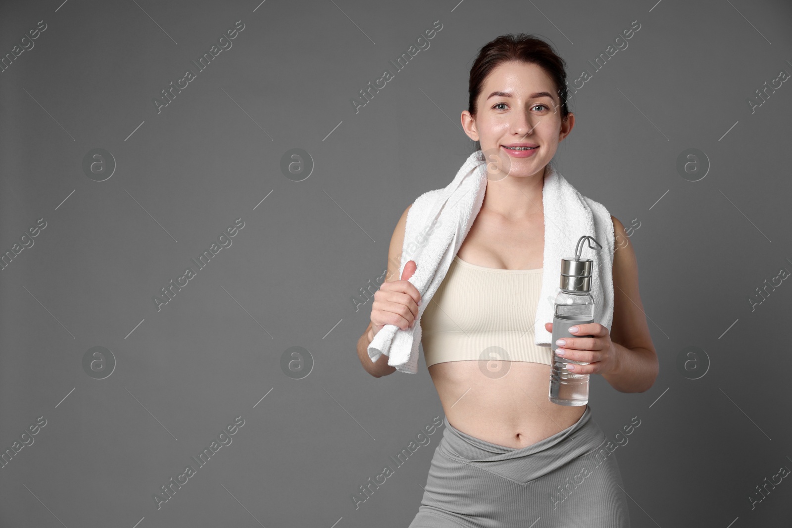 Photo of Woman in sportswear with bottle of water and towel on grey background, space for text