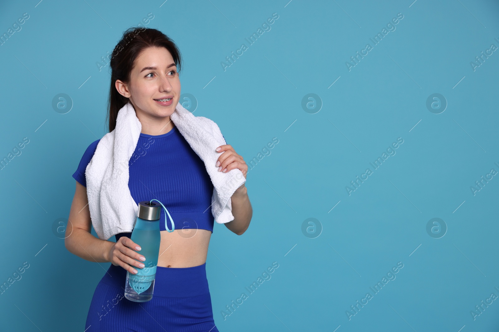 Photo of Woman in sportswear with bottle of water and towel on light blue background, space for text