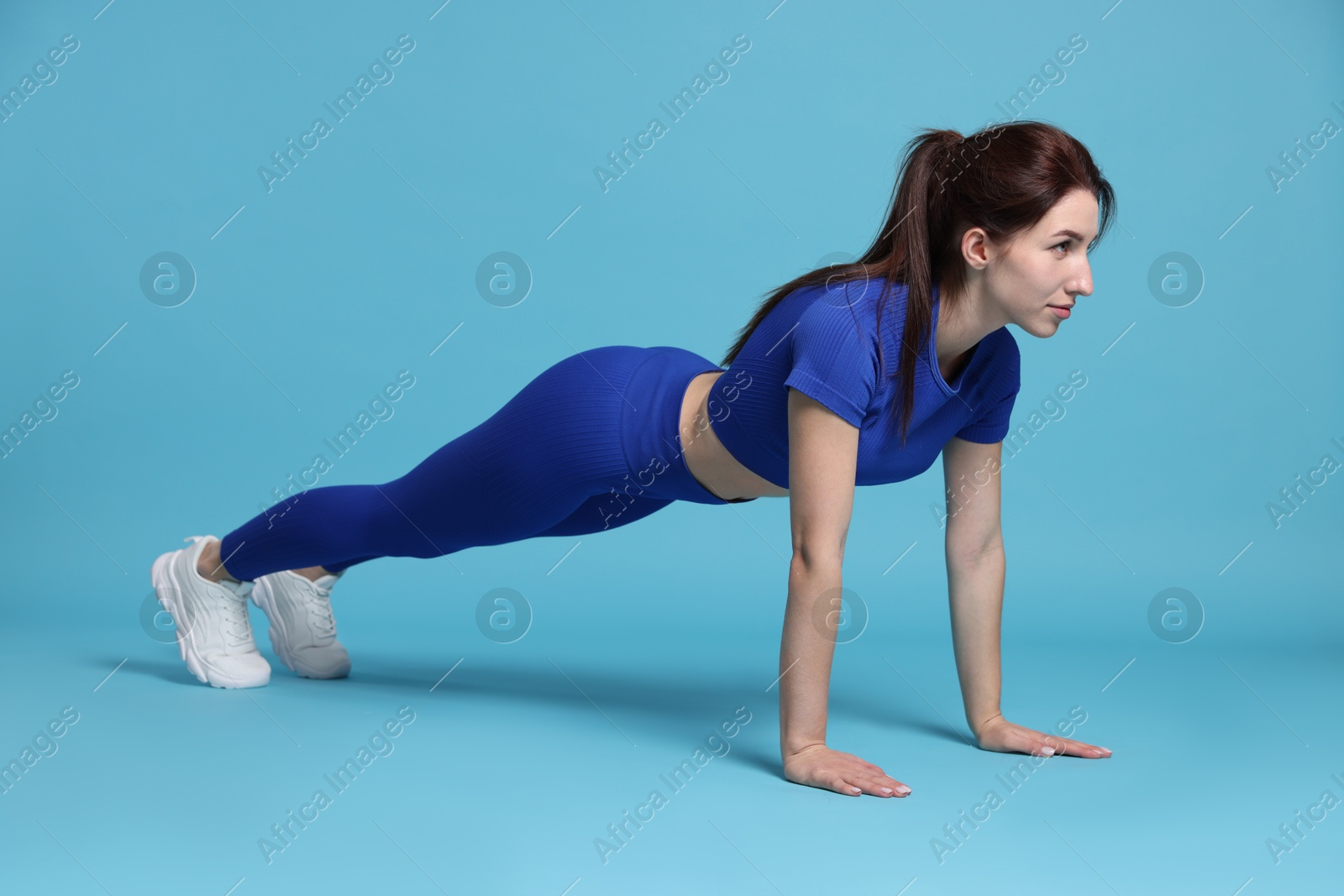 Photo of Woman in sportswear exercising on light blue background