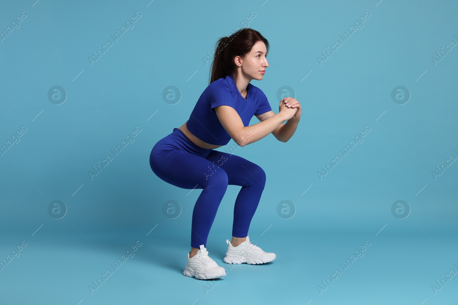 Photo of Woman in sportswear exercising on light blue background