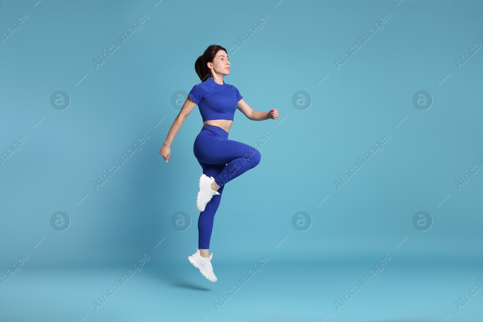 Photo of Woman in sportswear exercising on light blue background