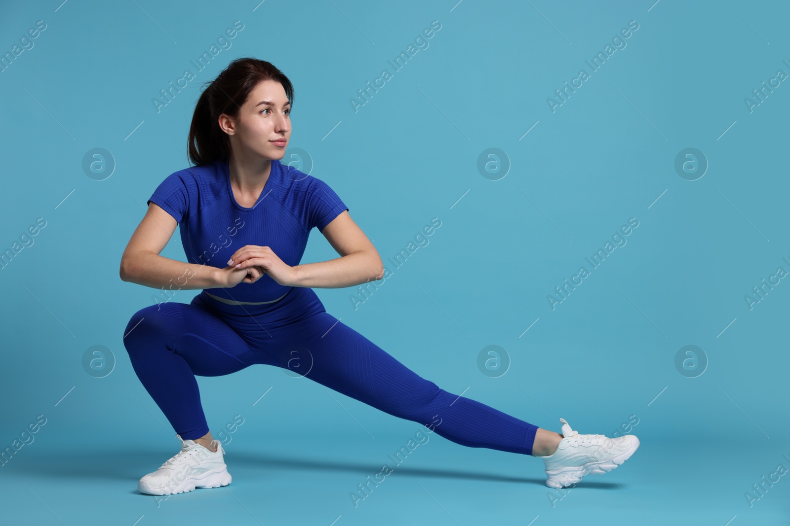 Photo of Woman in sportswear exercising on light blue background