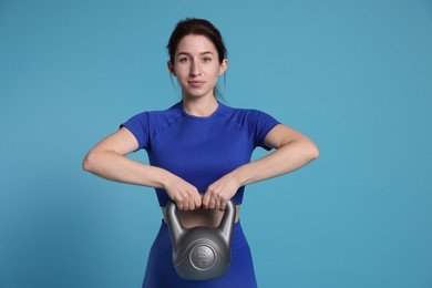 Photo of Woman in sportswear exercising with kettlebell on light blue background