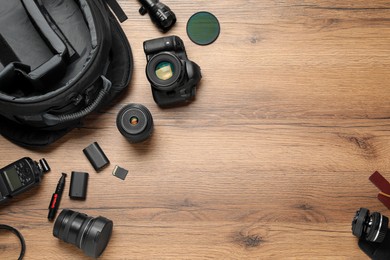 Photo of Professional photographer's equipment and backpack on wooden background, flat lay. Space for text