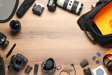 Photo of Frame of professional photographer's equipment and backpack on wooden background, flat lay. Space for text