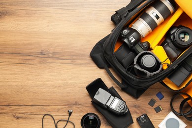 Photo of Professional photographer's equipment and backpack on wooden background, flat lay. Space for text