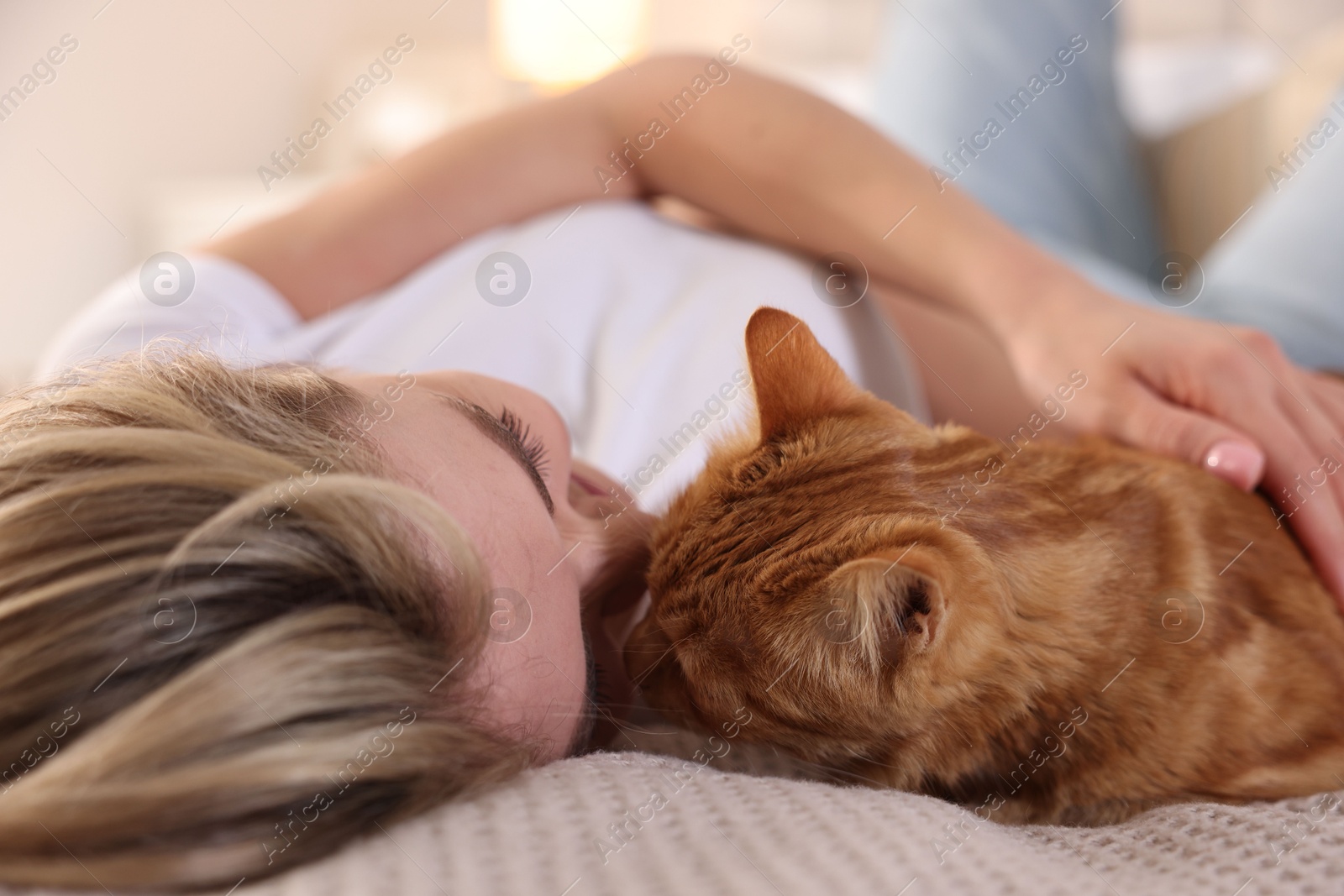 Photo of Woman with her cute ginger cat on bed at home