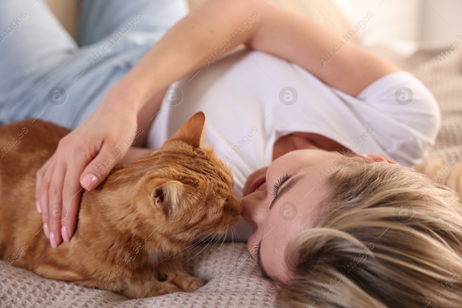 Photo of Woman with her cute ginger cat on bed at home