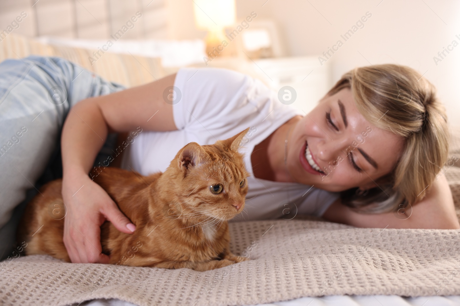 Photo of Woman with her cute ginger cat on bed at home