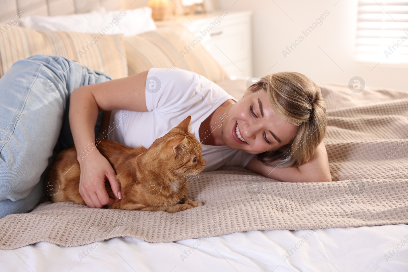 Photo of Woman with her cute ginger cat on bed at home