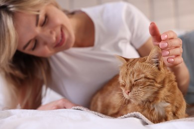 Photo of Woman stroking cute ginger cat on bed at home, selective focus