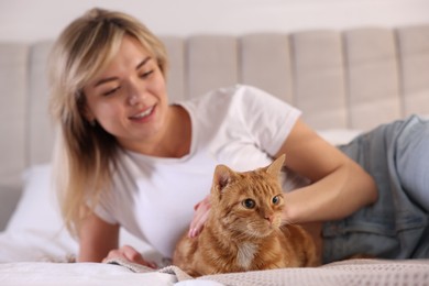 Photo of Woman stroking cute ginger cat on bed at home, selective focus