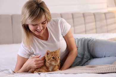 Photo of Woman stroking cute ginger cat on bed at home