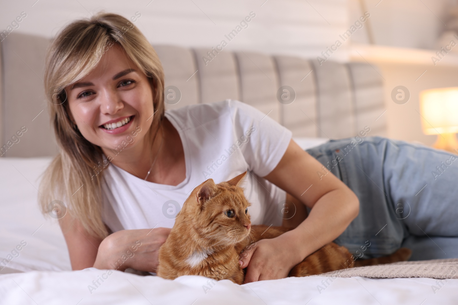 Photo of Woman with cute ginger cat on bed at home