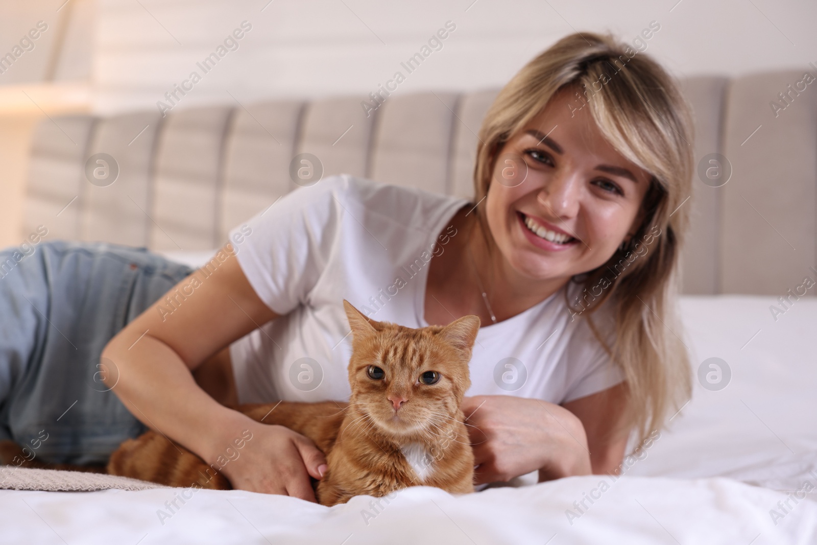 Photo of Woman with cute ginger cat on bed at home