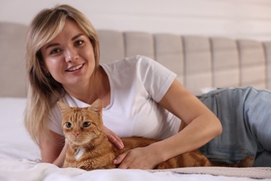 Photo of Woman with cute ginger cat on bed at home