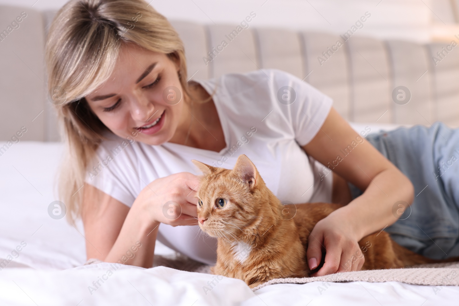 Photo of Woman stroking cute ginger cat on bed at home