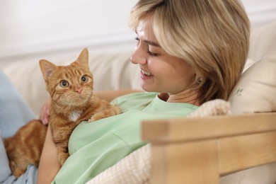 Photo of Woman with her cute ginger cat on sofa at home