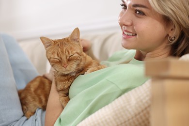 Photo of Woman with her cute ginger cat on sofa at home