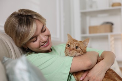 Photo of Woman with her cute ginger cat on sofa at home