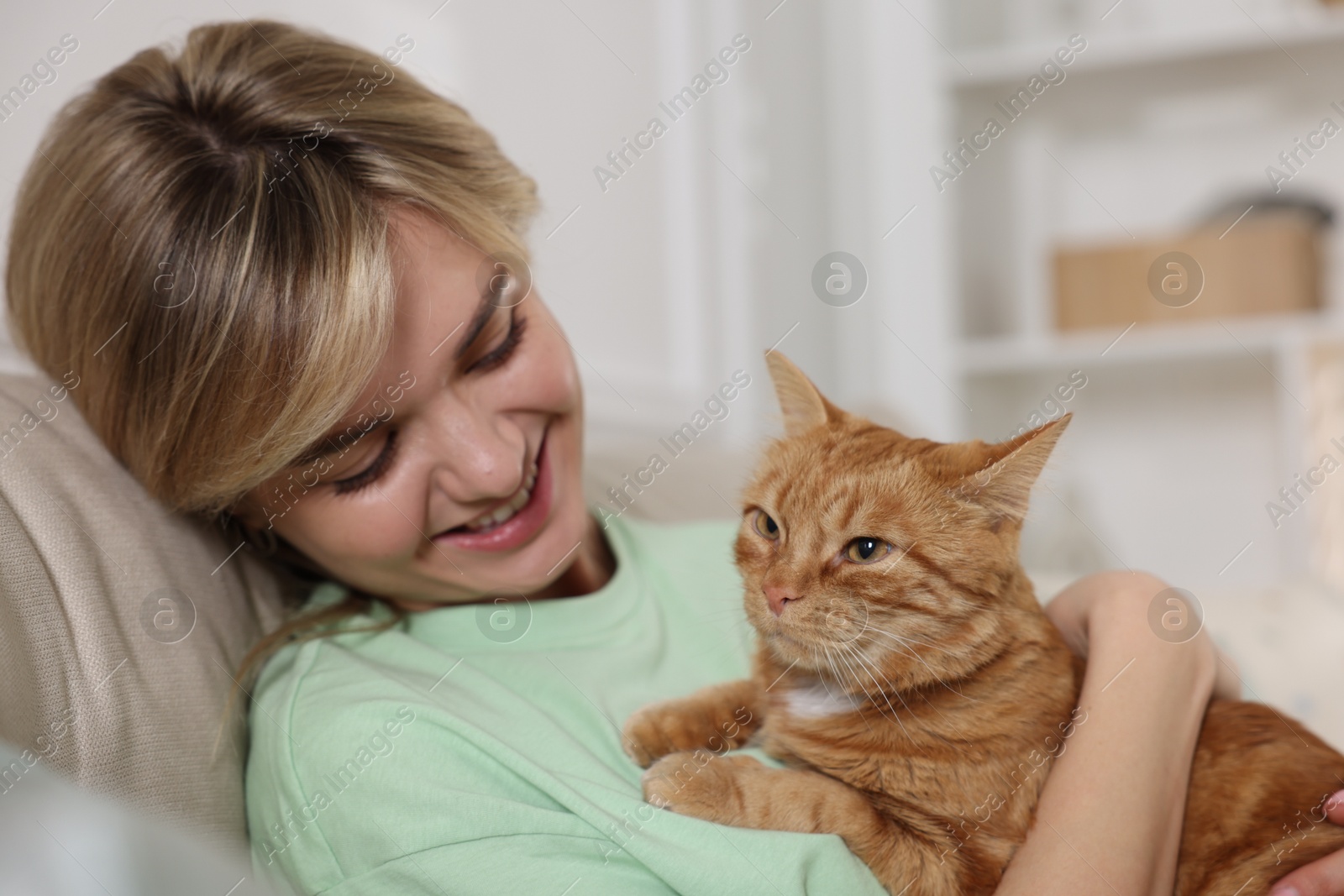 Photo of Woman with her cute ginger cat on sofa at home