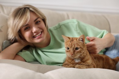 Photo of Woman stroking cute ginger cat on sofa at home, selective focus