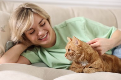 Photo of Woman stroking cute ginger cat on sofa at home, selective focus