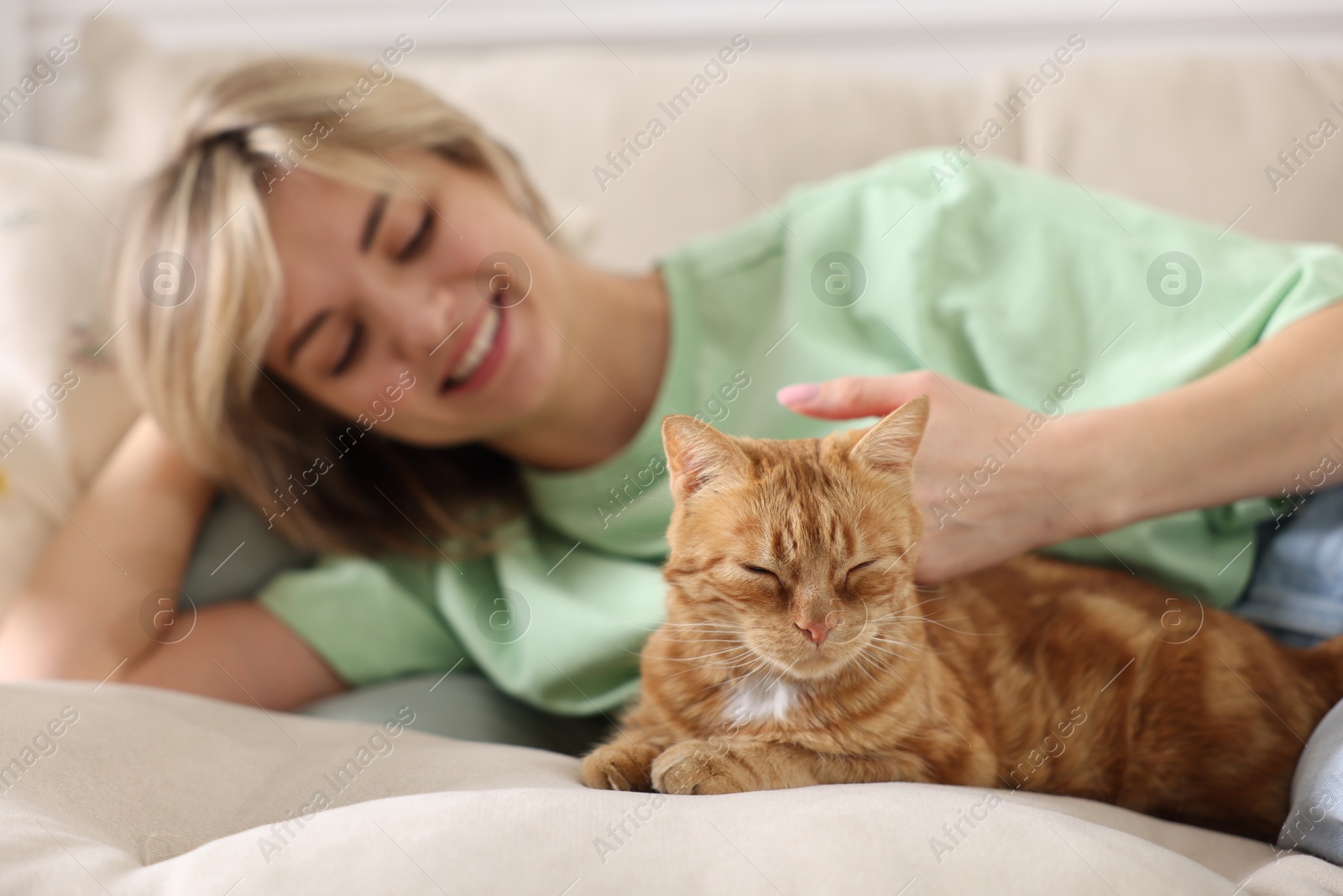 Photo of Woman stroking cute ginger cat on sofa at home, selective focus