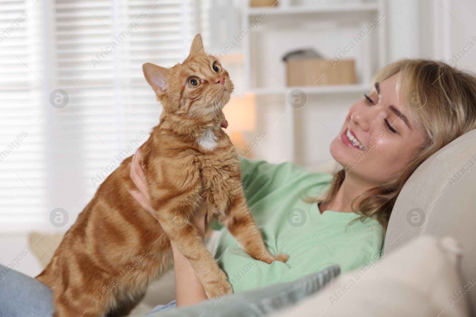 Photo of Woman with her cute ginger cat on sofa at home