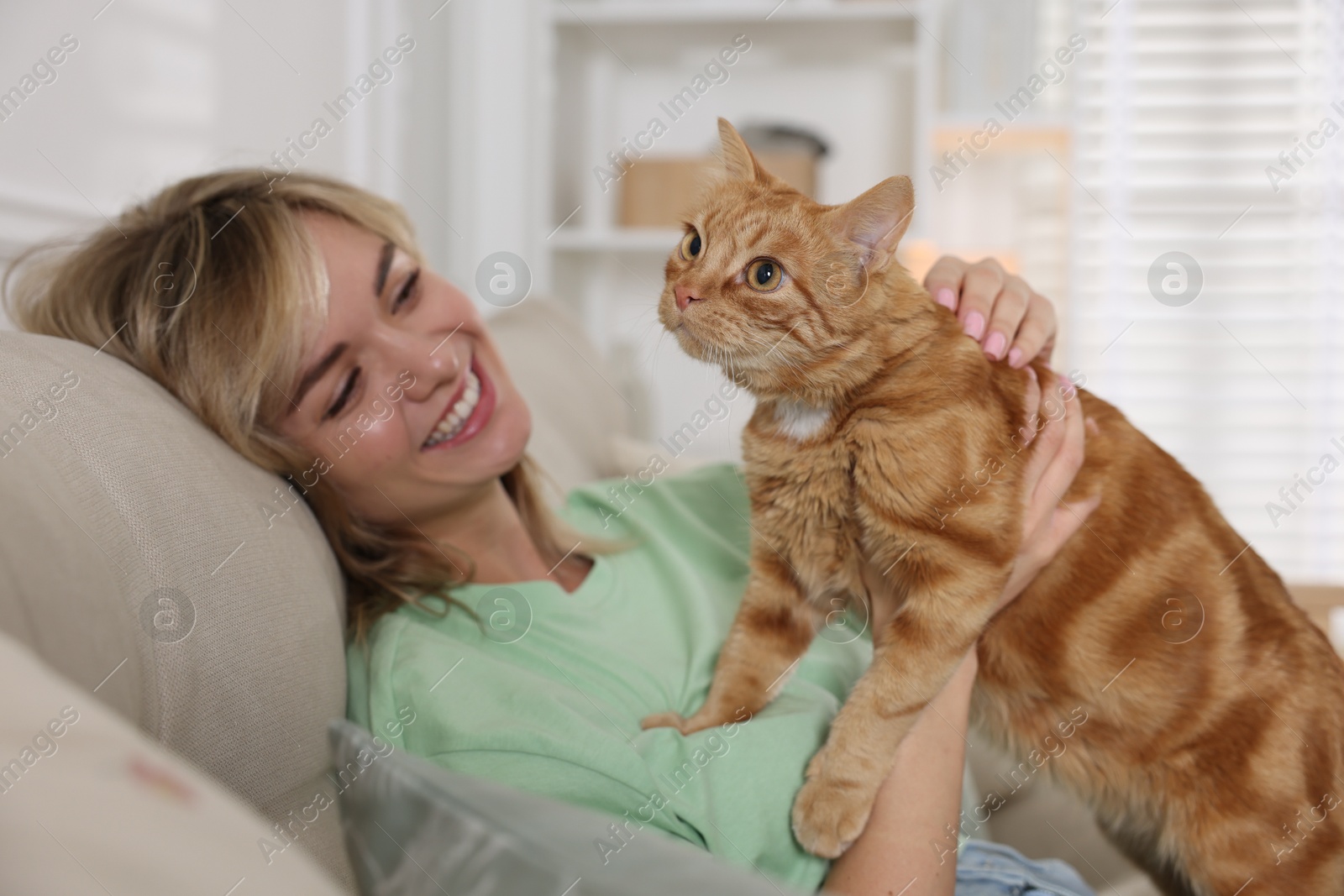 Photo of Woman with her cute ginger cat on sofa at home