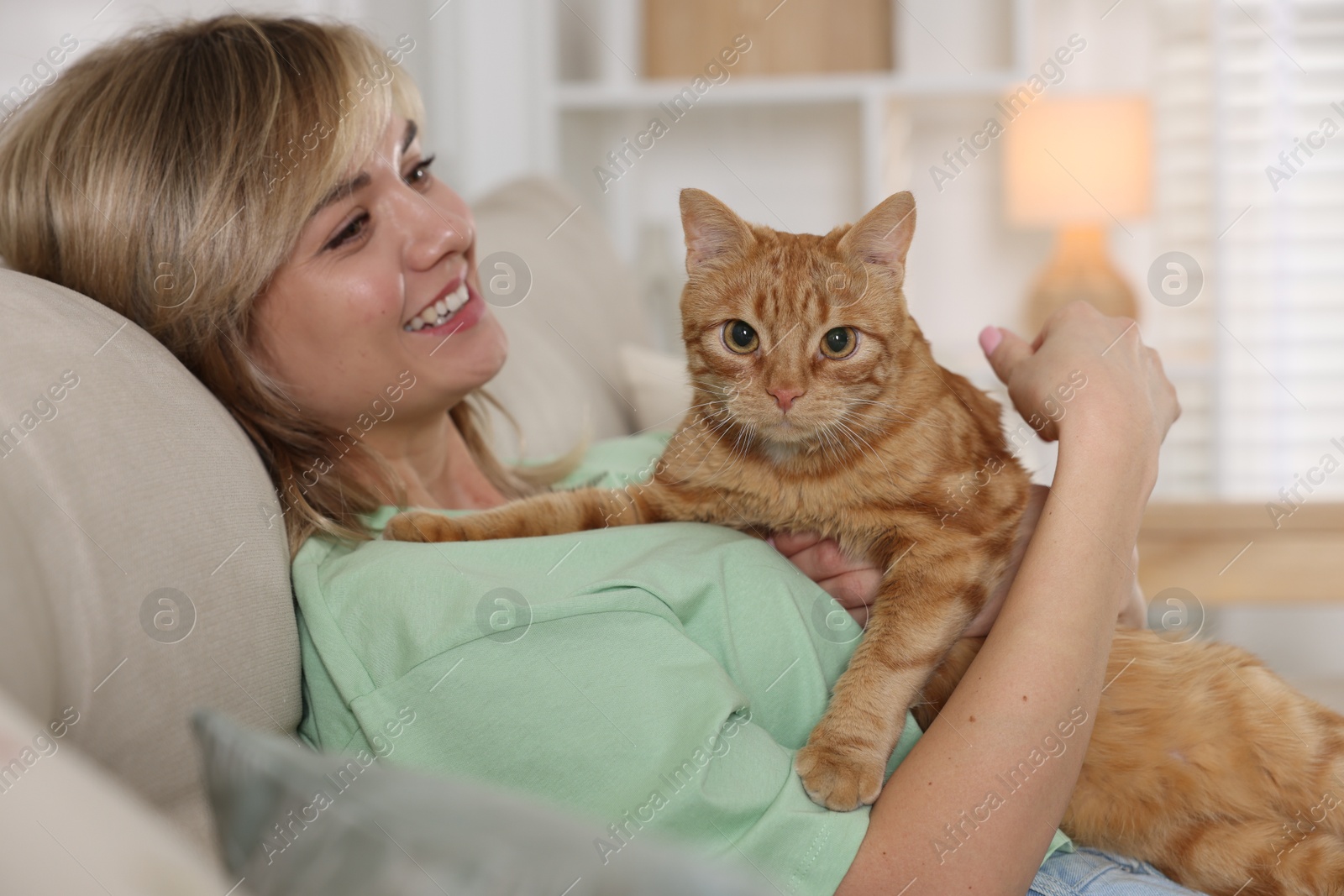 Photo of Woman with her cute ginger cat on sofa at home