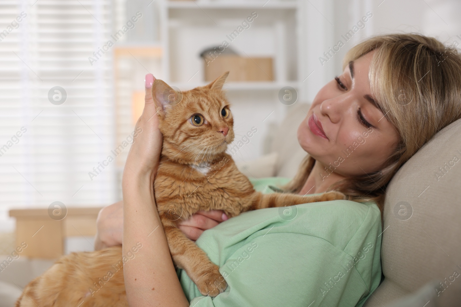 Photo of Woman with her cute ginger cat on sofa at home