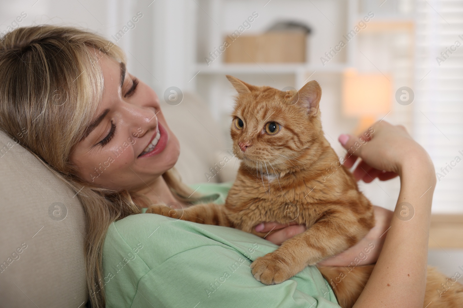 Photo of Woman with her cute ginger cat on sofa at home