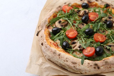 Photo of Tasty pizza with cherry tomatoes, black olives, mushrooms and arugula on white table, closeup. Space for text