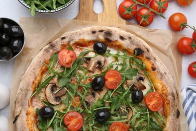 Photo of Tasty pizza with cherry tomatoes, black olives, mushrooms and arugula on light grey table, flat lay