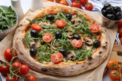 Photo of Tasty pizza with cherry tomatoes, black olives, mushrooms and arugula on table, closeup