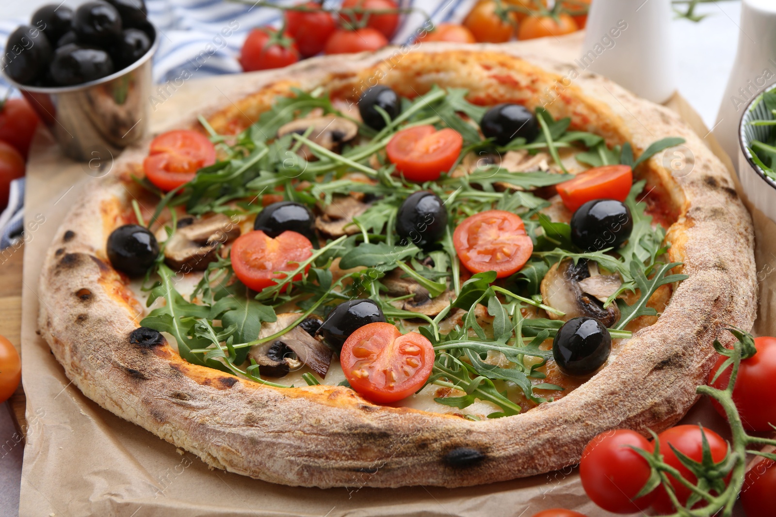 Tasty pizza with cherry tomatoes, black olives, mushrooms and arugula on table, closeup Photo of Tasty pizza with cherry tomatoes, black olives, mushrooms and arugula on table, closeup