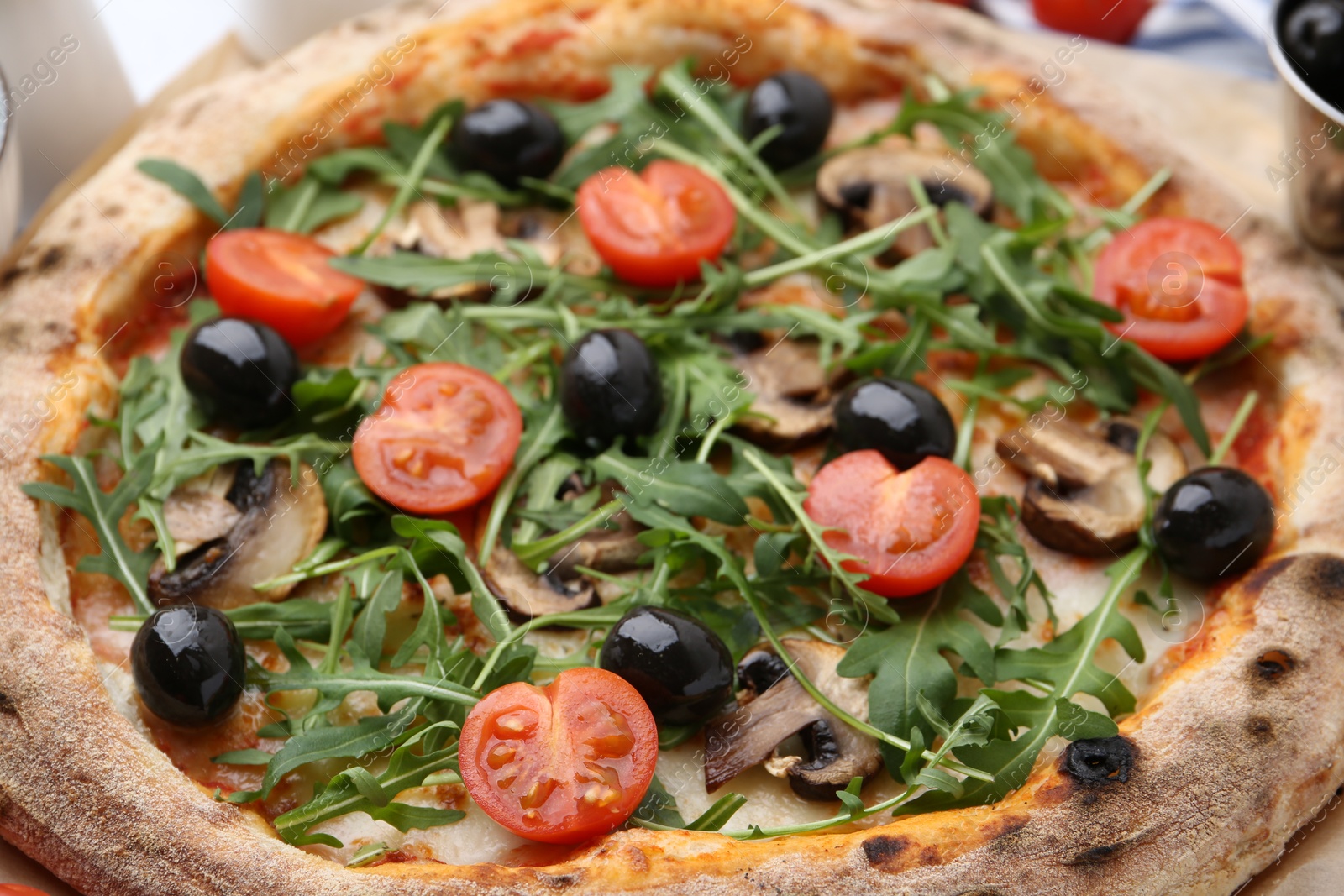 Tasty pizza with cherry tomatoes, black olives, mushrooms and arugula on table, closeup Photo of Tasty pizza with cherry tomatoes, black olives, mushrooms and arugula on table, closeup