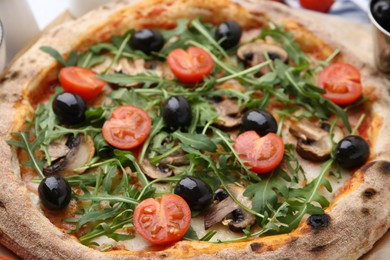 Photo of Tasty pizza with cherry tomatoes, black olives, mushrooms and arugula on table, closeup