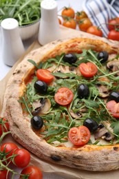 Photo of Tasty pizza with cherry tomatoes, black olives, mushrooms and arugula on table, closeup